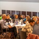 A diverse group of conference attendees seated at tables in a large hall, listening attentively to the conversational AI tech summit
